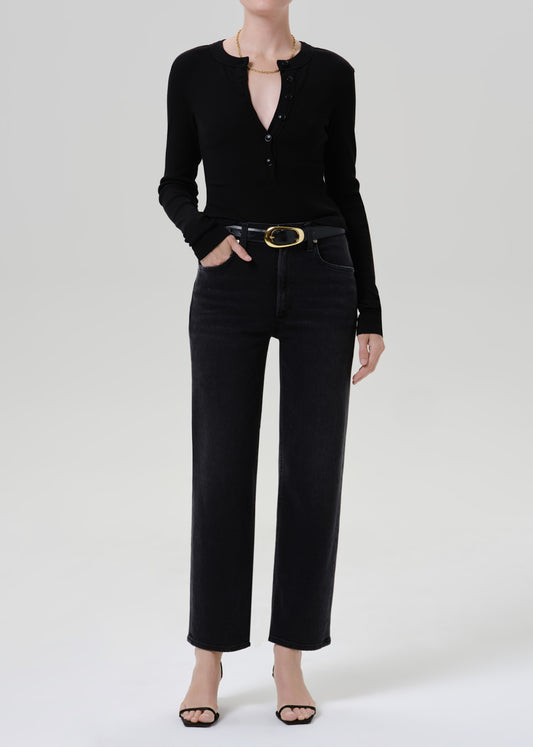 Person wearing a black long sleeve henley top with black straight leg jeans on a grey background