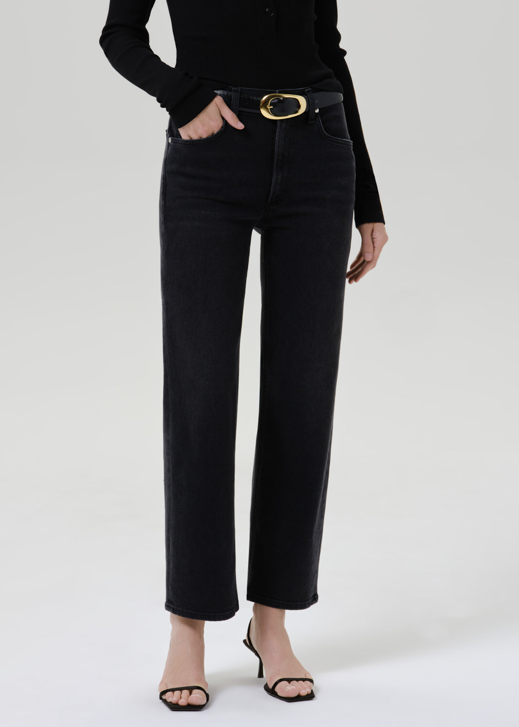 Person wearing a black long sleeve henley top with black straight leg jeans on a grey background