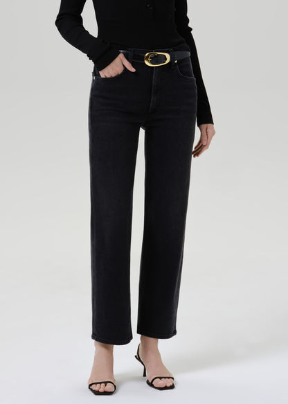 Person wearing a black long sleeve henley top with black straight leg jeans on a grey background