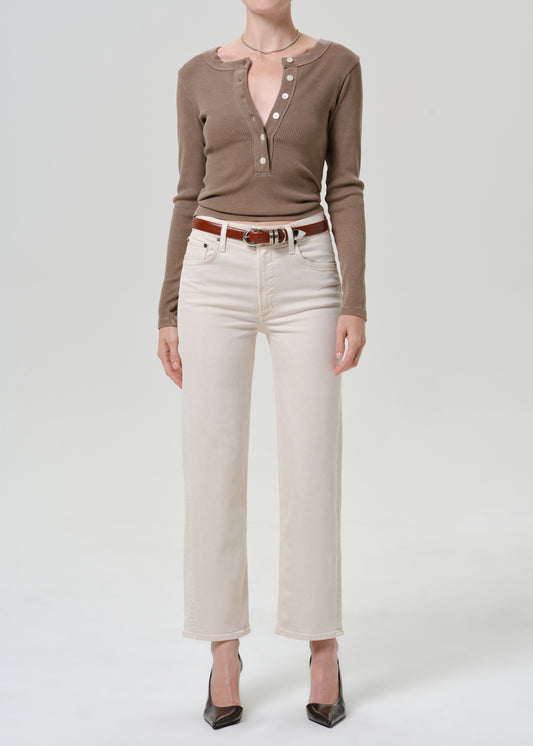 Person wearing cream cropped wide leg jeans with a taupe long sleeve button-front top, brown belt, and black pointed-toe heels, front full body view on a grey background.