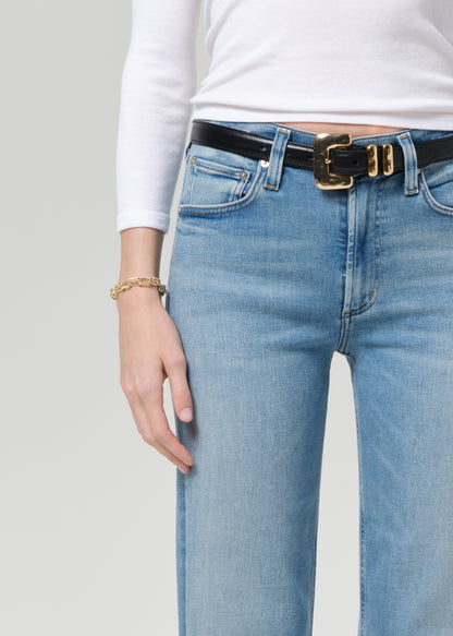 Person wearing light blue jeans with a black belt and gold buckle on a plain background