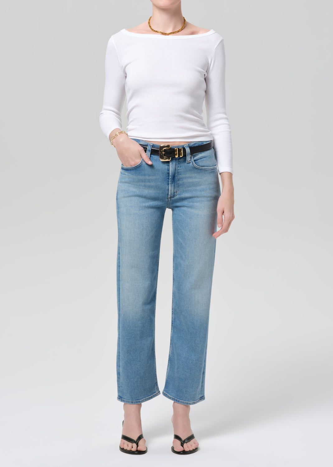 Person wearing a white long-sleeve top and light blue jeans on a plain background