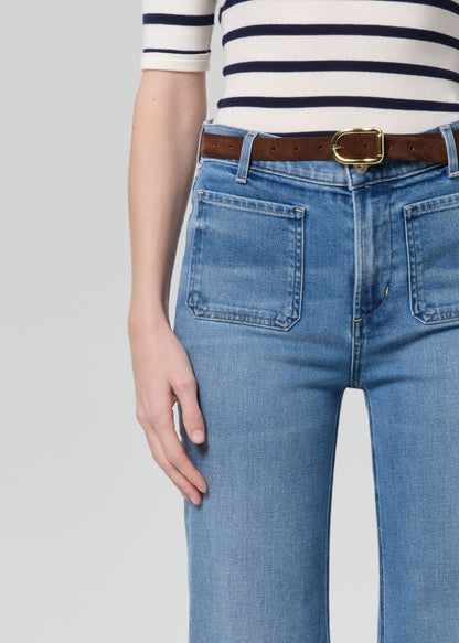 Person wearing blue jeans with a brown belt and white and navy striped shirt on a light gray background