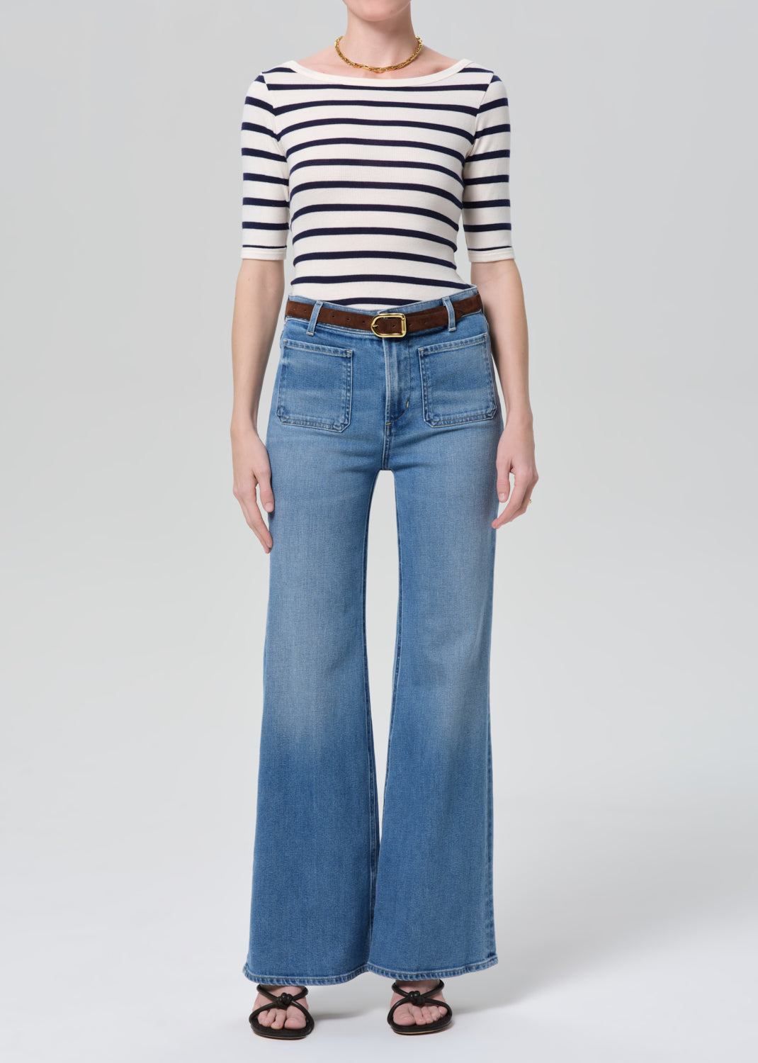 Person wearing a striped shirt and blue jeans on a grey background