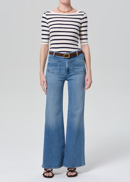 Person wearing a striped shirt and blue jeans on a grey background
