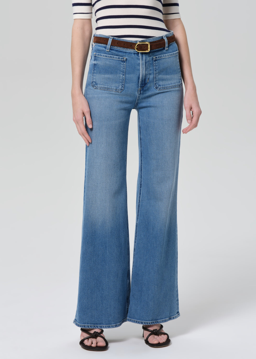 Person wearing blue jeans and a striped shirt on a grey background