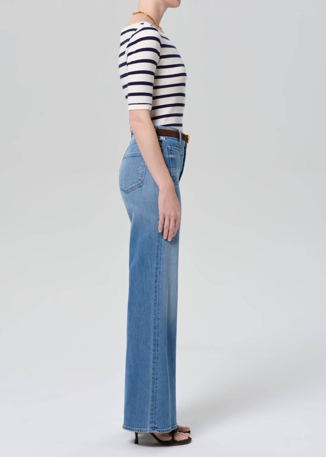 Person wearing a striped shirt and blue jeans on a grey background