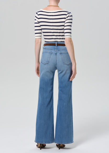 Person wearing a striped shirt and blue jeans on a grey background