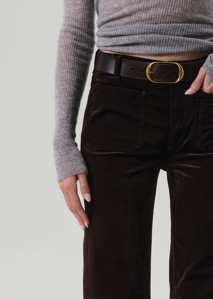 Person wearing a gray sweater and brown pants with a gold belt buckle on a light gray background