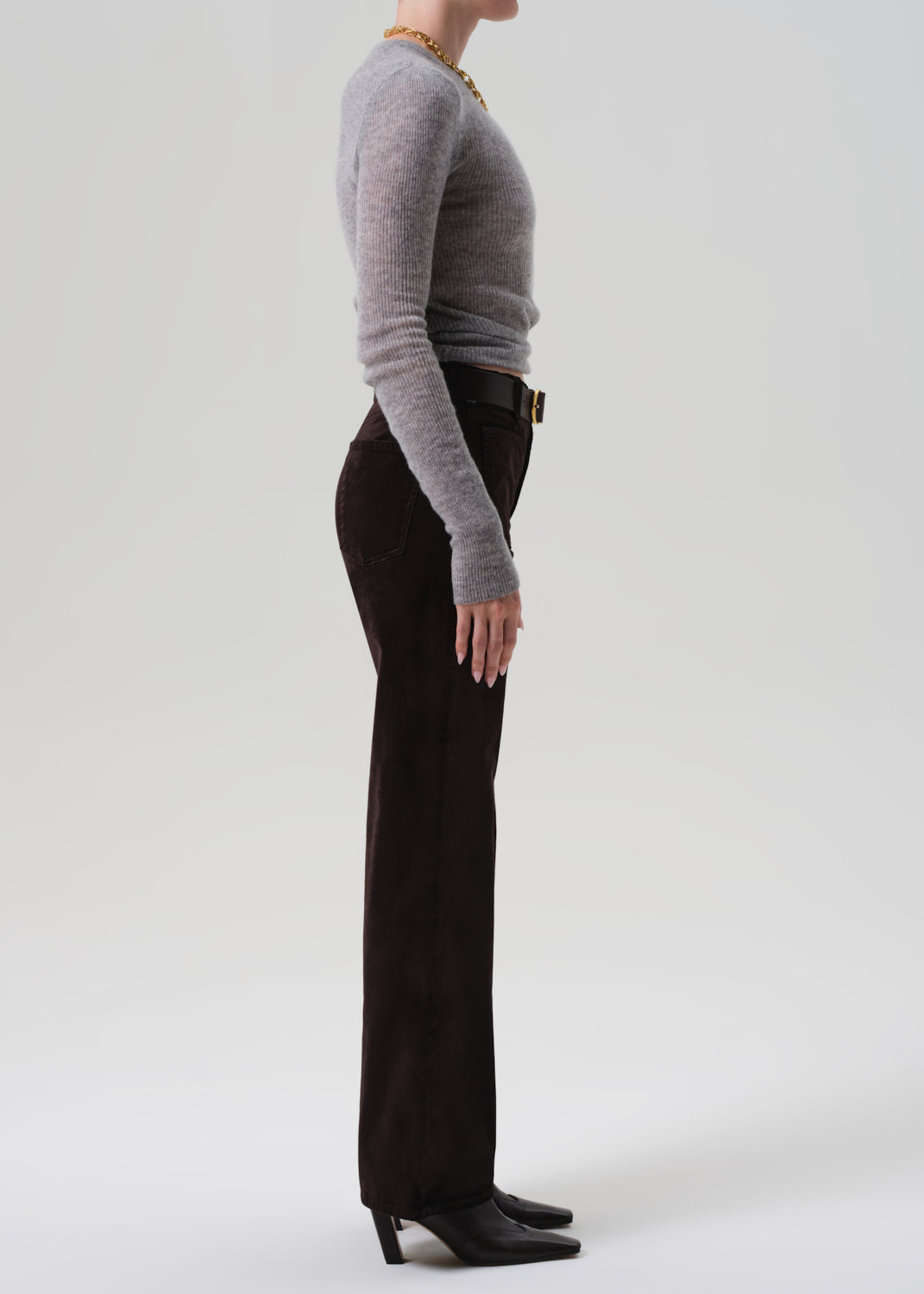 Person wearing a gray sweater and black pants on a white background