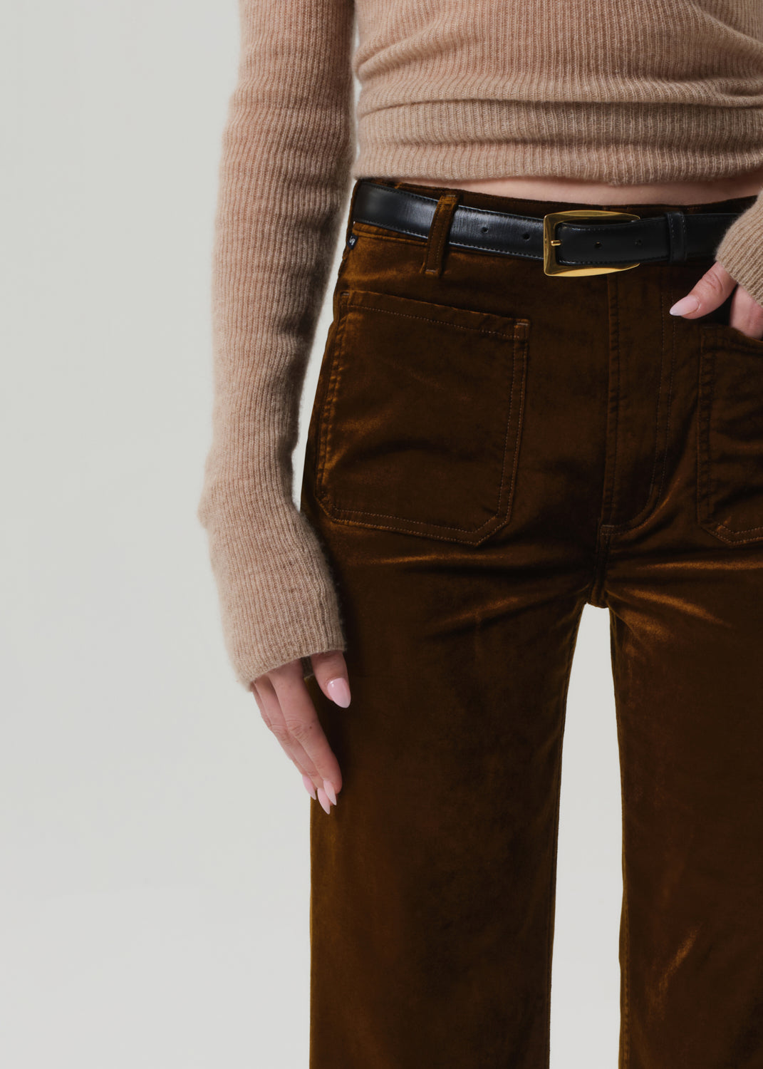 Person wearing a beige sweater and brown velvet flare-leg pants on a grey background