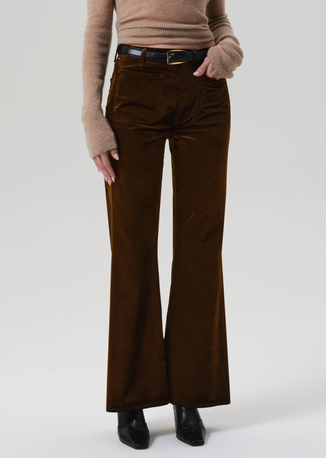 Person wearing a beige sweater and brown velvet flare-leg pants on a grey background