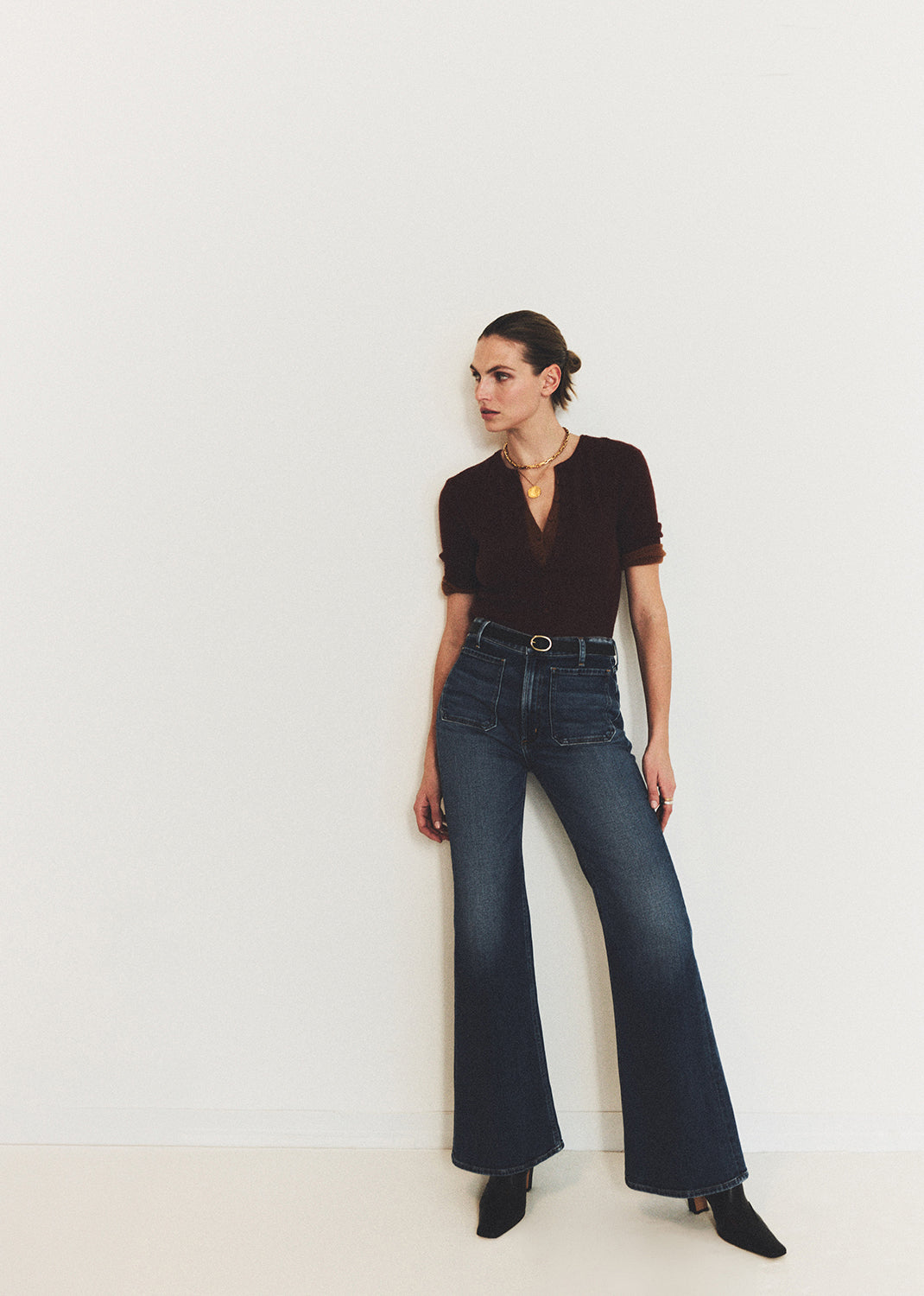 Woman wearing a brown top and blue jeans against a grey background