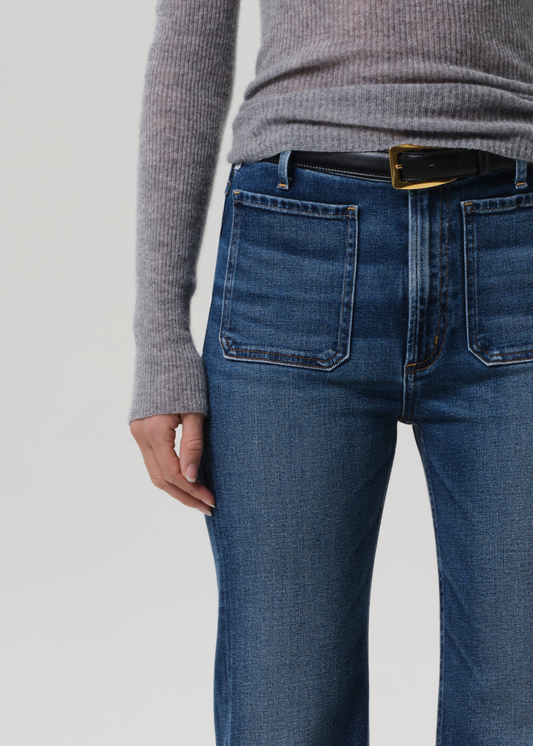 Person wearing blue jeans and a gray sweater on a plain background