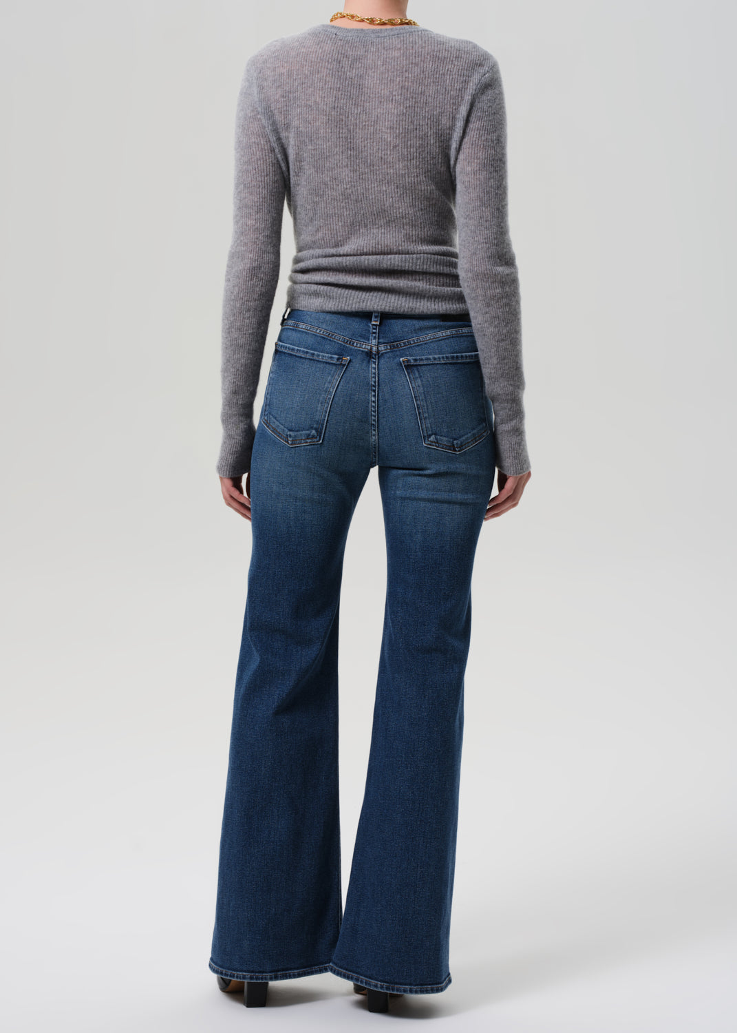 Person wearing a gray sweater and blue flared jeans on a white background