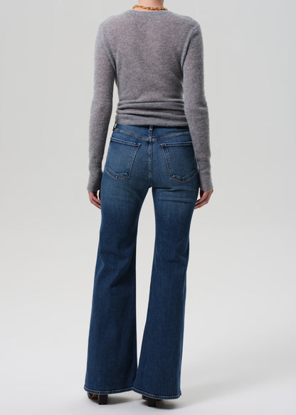 Person wearing a gray sweater and blue flared jeans on a white background