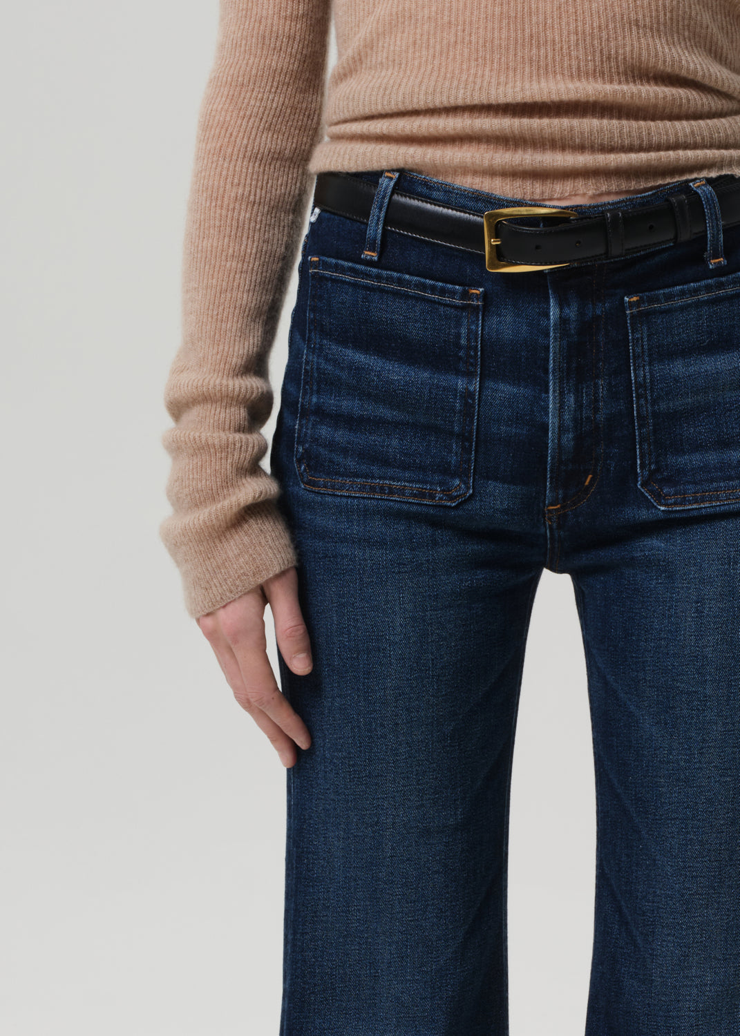 Person wearing blue jeans and a beige sweater with a plain background