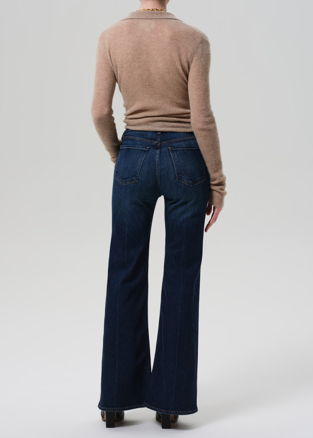 Person wearing a beige sweater and dark blue flared jeans on a white background