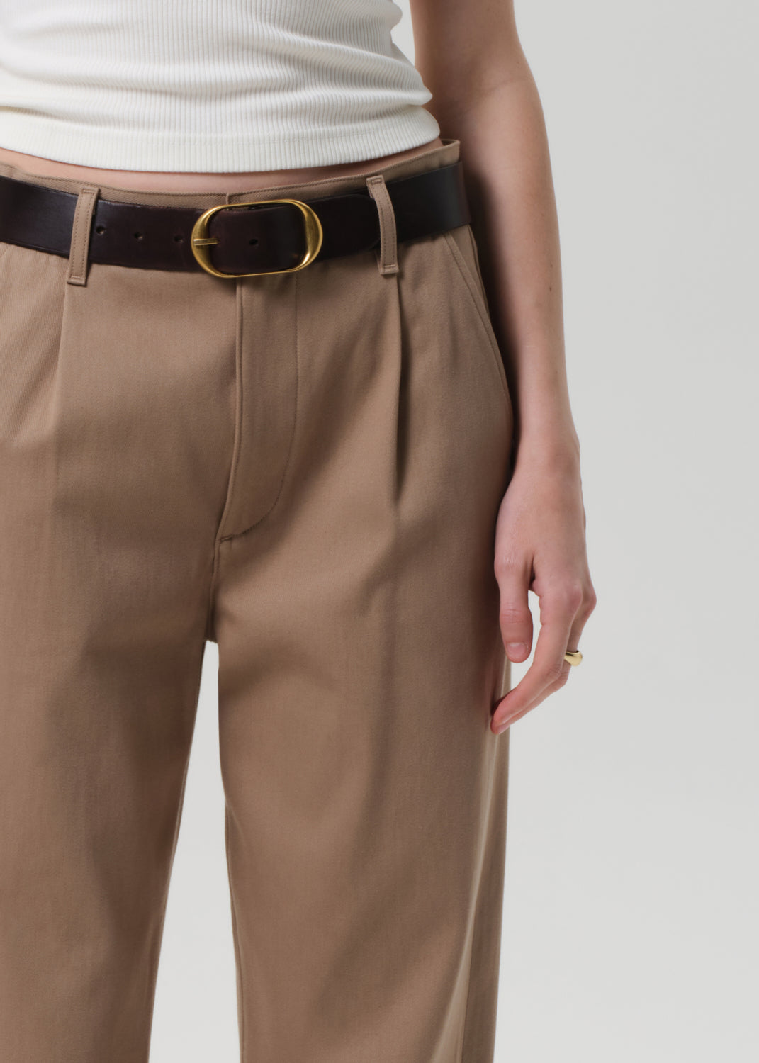 Person wearing beige pants with a black belt on a plain background