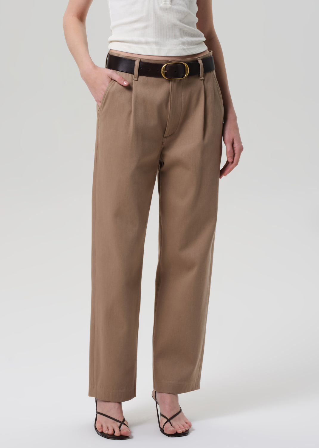 Person wearing beige pants with a belt on a white background
