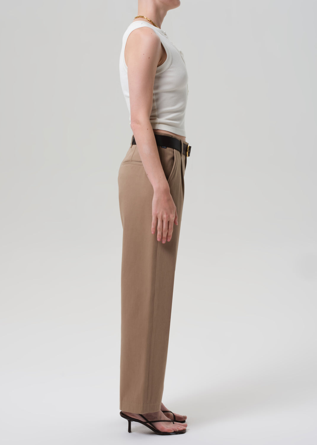Person wearing a white sleeveless top and beige pants on a plain background