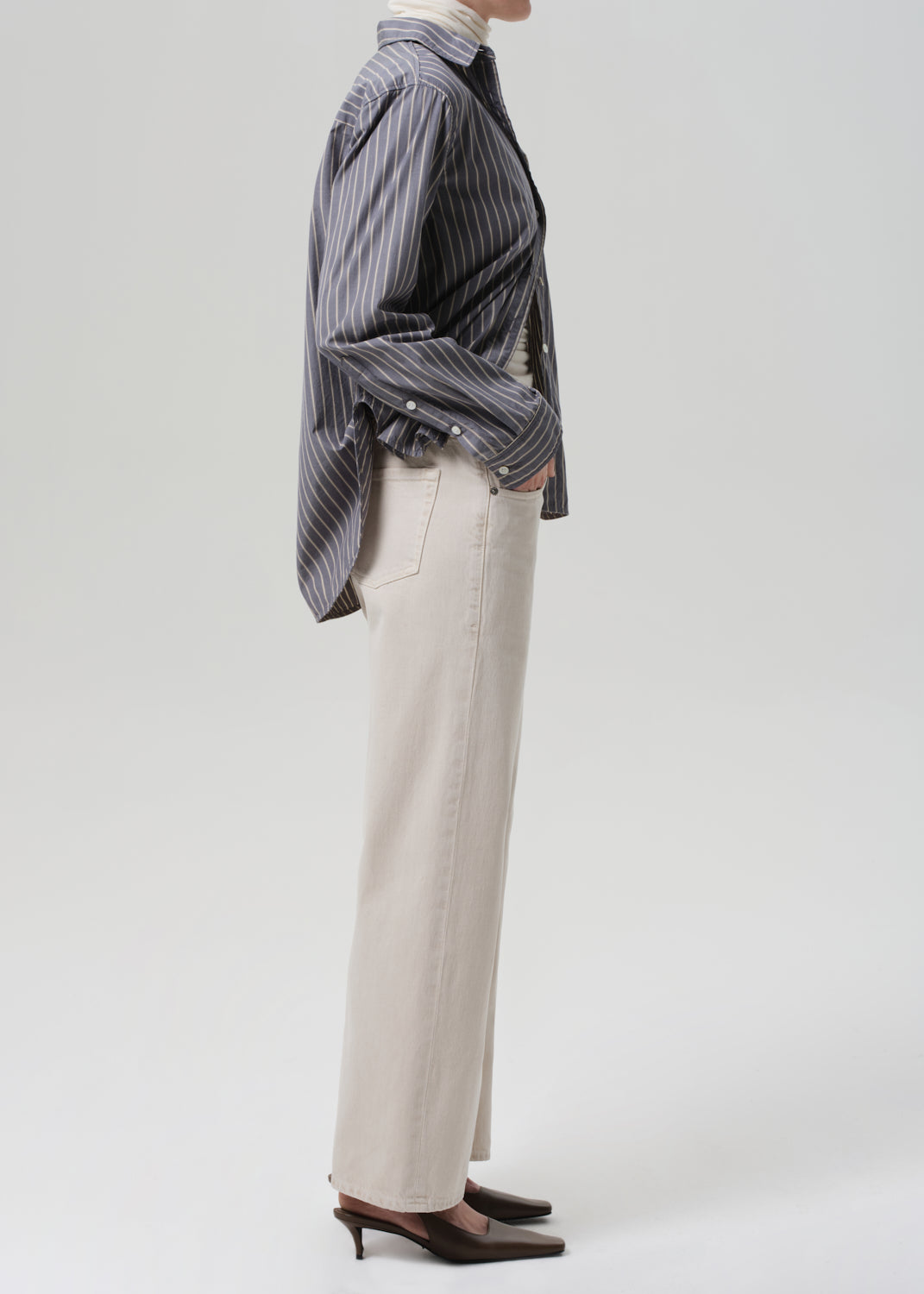 Person wearing a striped shirt and beige pants on a white background