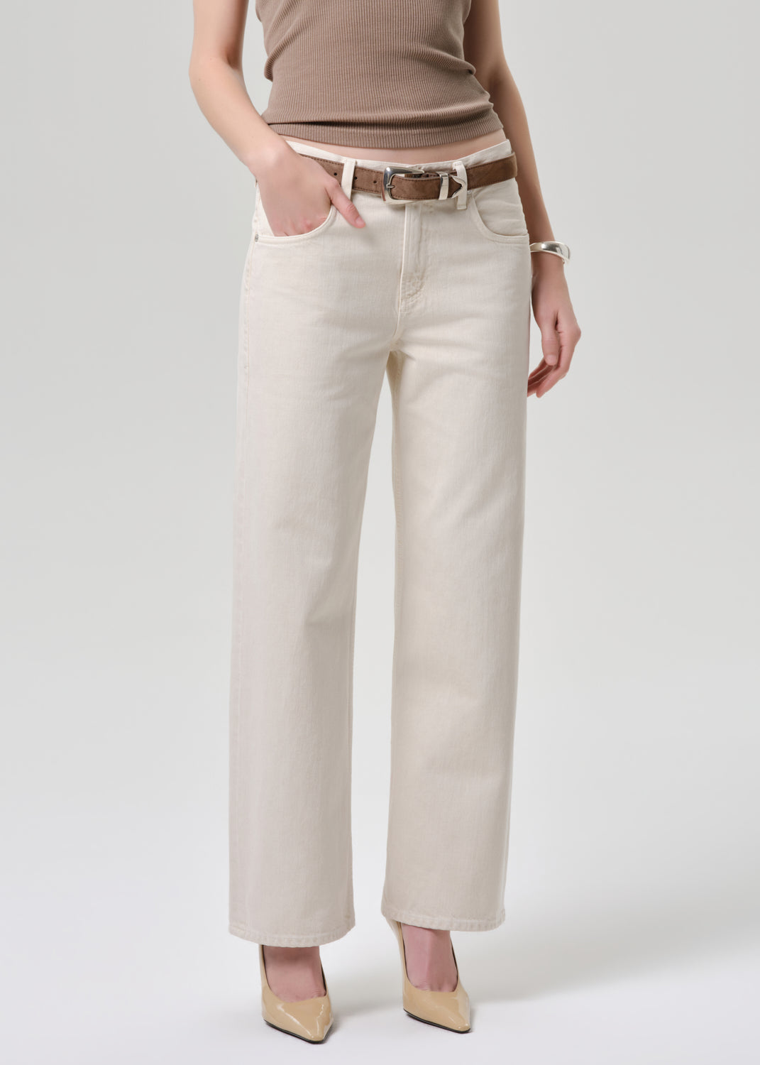 A model wearing off-white wide-leg cropped jeans with a brown leather belt, paired with a taupe top and beige heels, against a grey background.