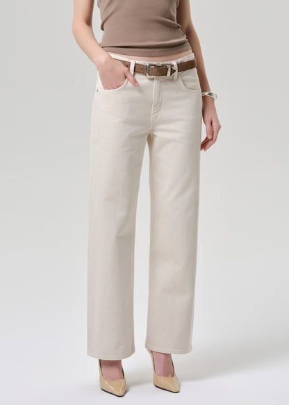 A model wearing off-white wide-leg cropped jeans with a brown leather belt, paired with a taupe top and beige heels, against a grey background.
