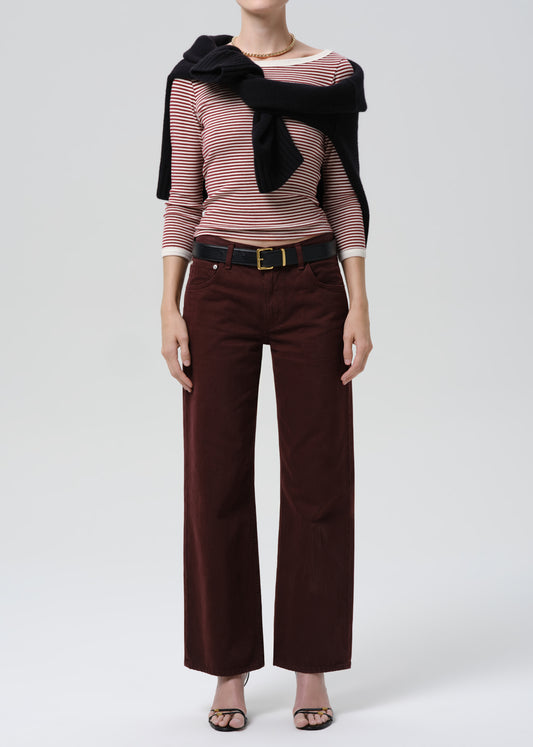 Person wearing a striped sweater with a black sweater and burgundy pants on a grey background