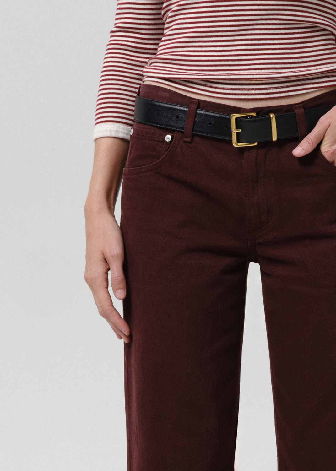 Person wearing a striped shirt and burgundy pants with a black belt on a grey background