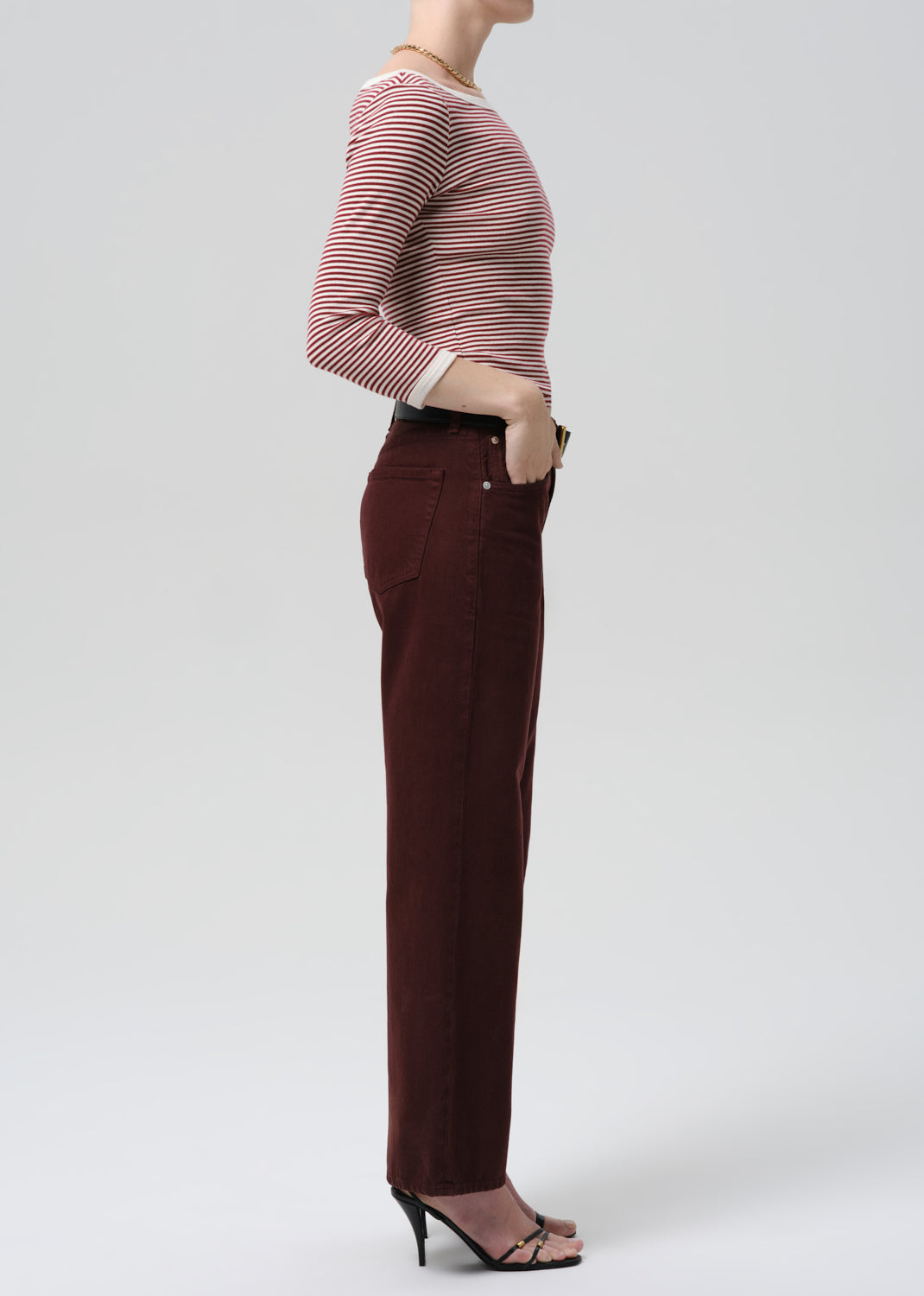 Person wearing a striped sweater and burgundy pants on a grey background