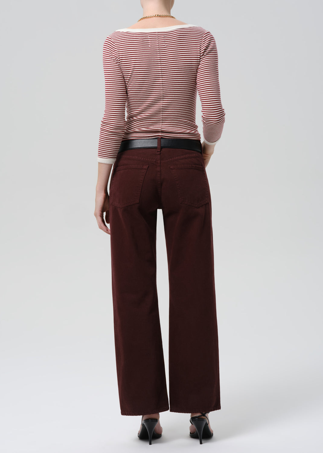 Person wearing a striped shirt and brown pants on a grey background