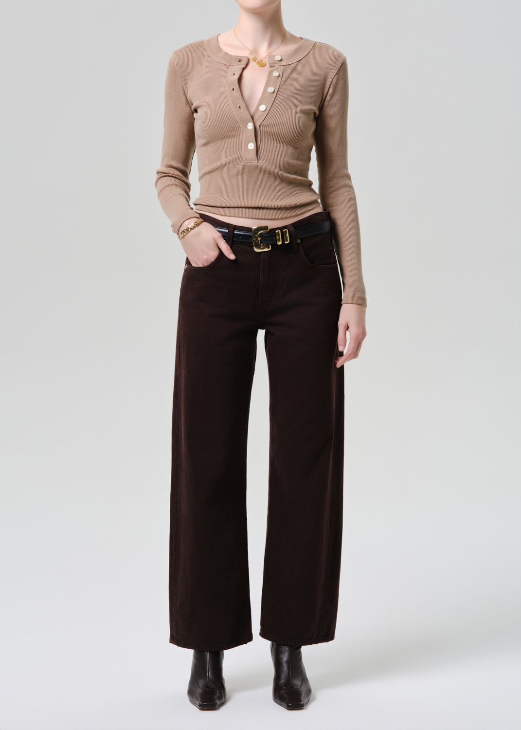 Person wearing a brown long-sleeve top and dark brown wide-leg pants on a grey background
