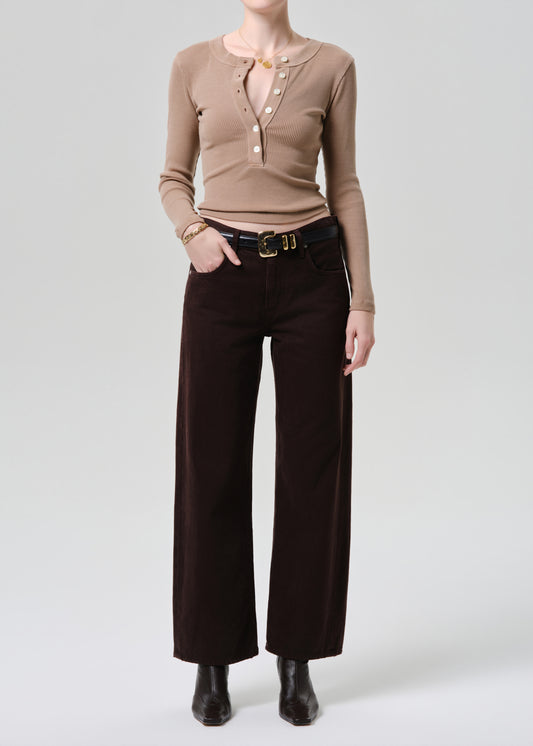 Person wearing a brown long-sleeve top and dark brown wide-leg pants on a grey background