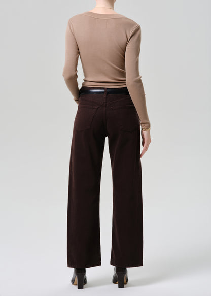 A model shown from the back wearing a beige long-sleeve top and dark brown wide-leg trousers, paired with a black belt and black heels, against a grey background.
