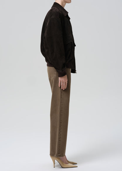 Person wearing a dark brown jacket and beige pants on a grey background