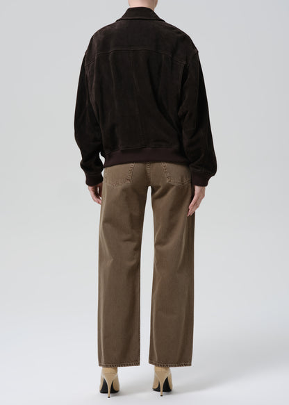 Person wearing a dark brown jacket and beige pants on a grey background