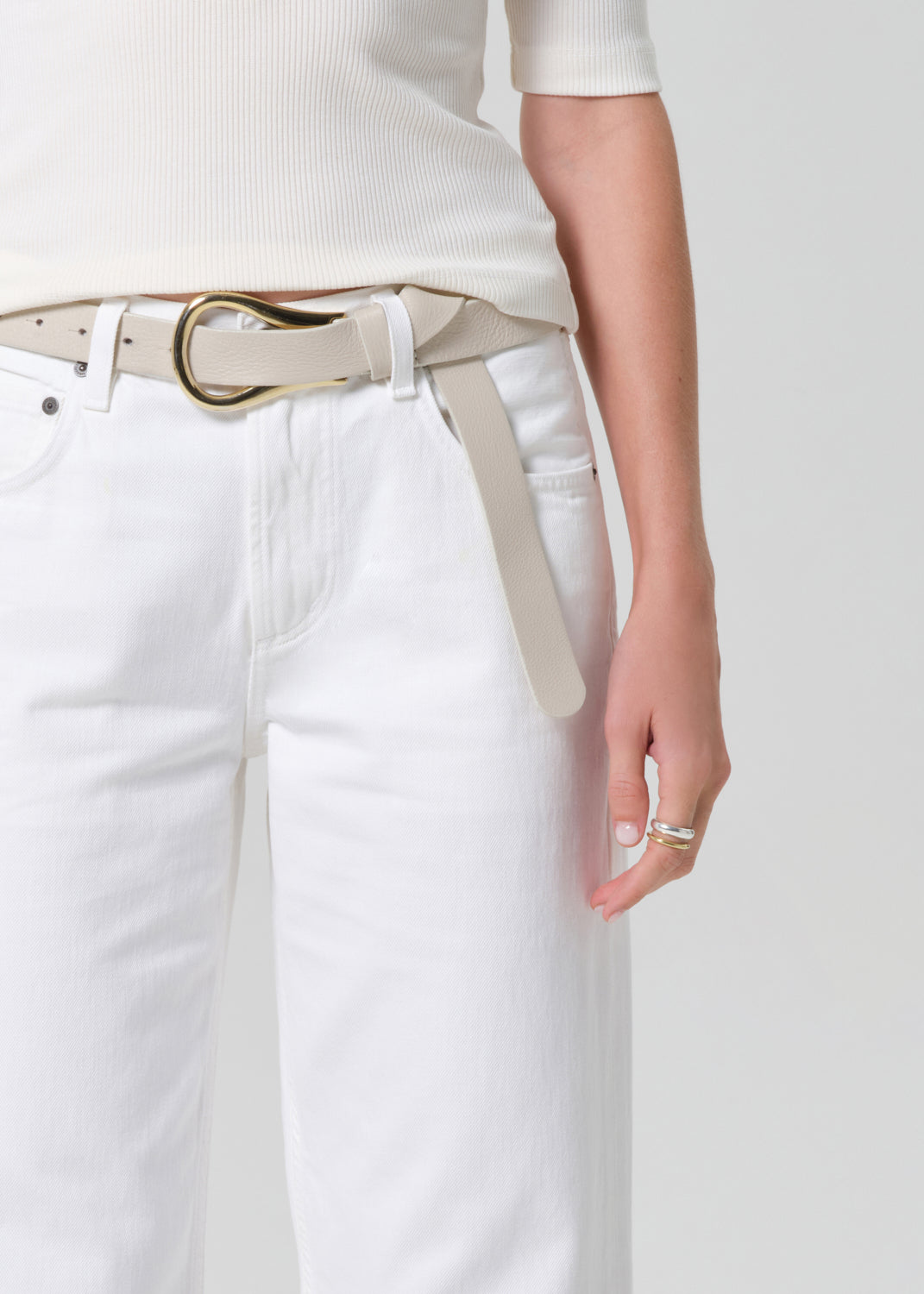 Person wearing a white shirt and white jeans with a belt on a plain background