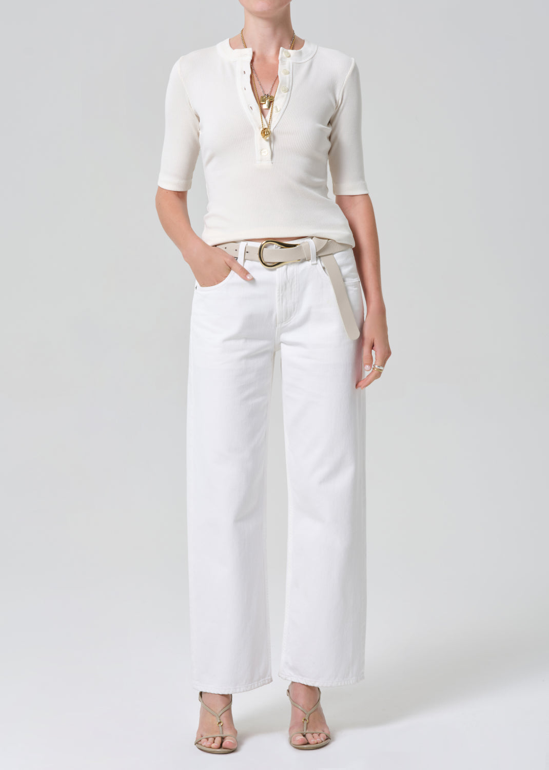 Person wearing a white shirt and white jeans with a belt on a plain background