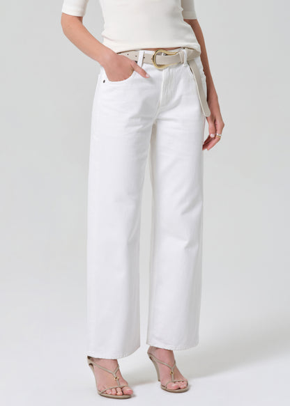 Person wearing a white shirt and white jeans with a belt on a plain background