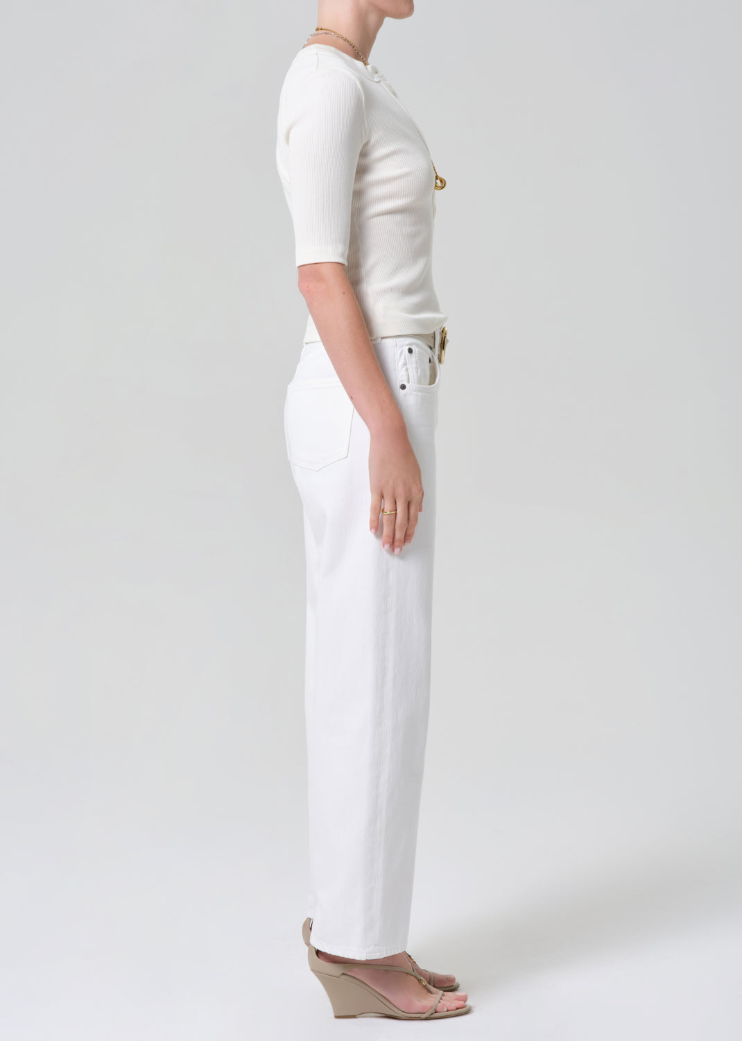 Person wearing a white shirt and white jeans with a belt on a plain background