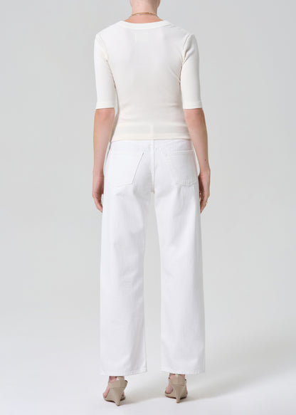 Person wearing a white shirt and white jeans with a belt on a plain background