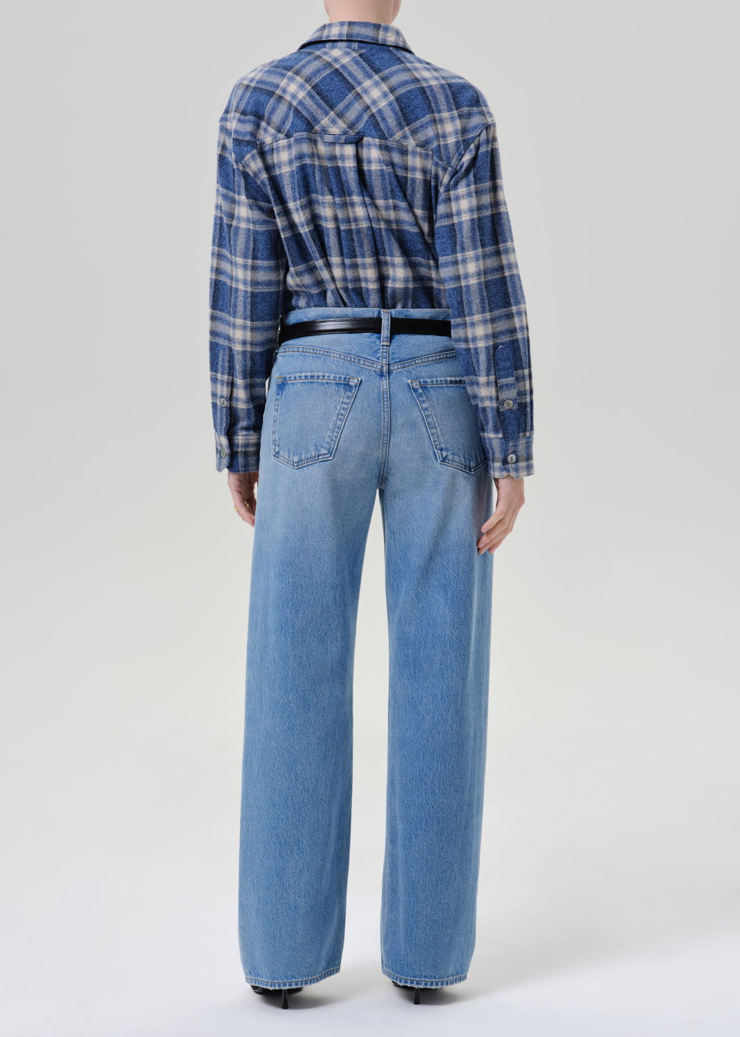 A model shown from the back wearing a blue and white plaid button-down shirt tucked into light-wash wide-leg denim jeans with a black belt.