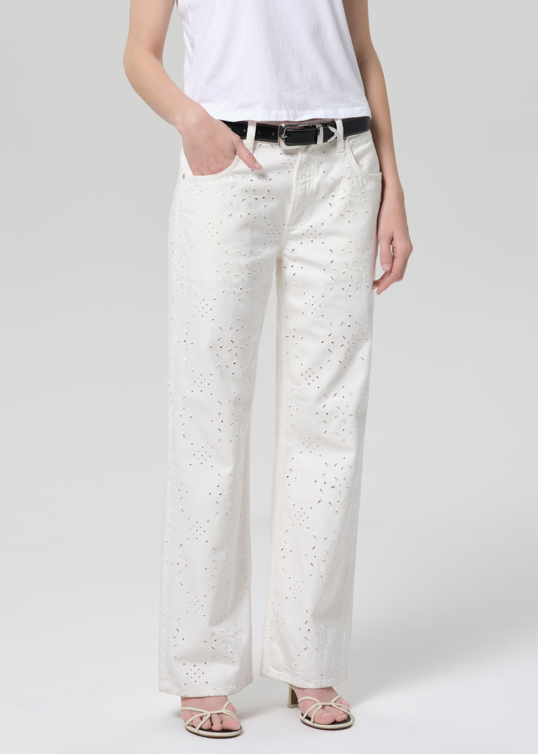 Person wearing a white t-shirt and white jeans with eyelet on a plain background
