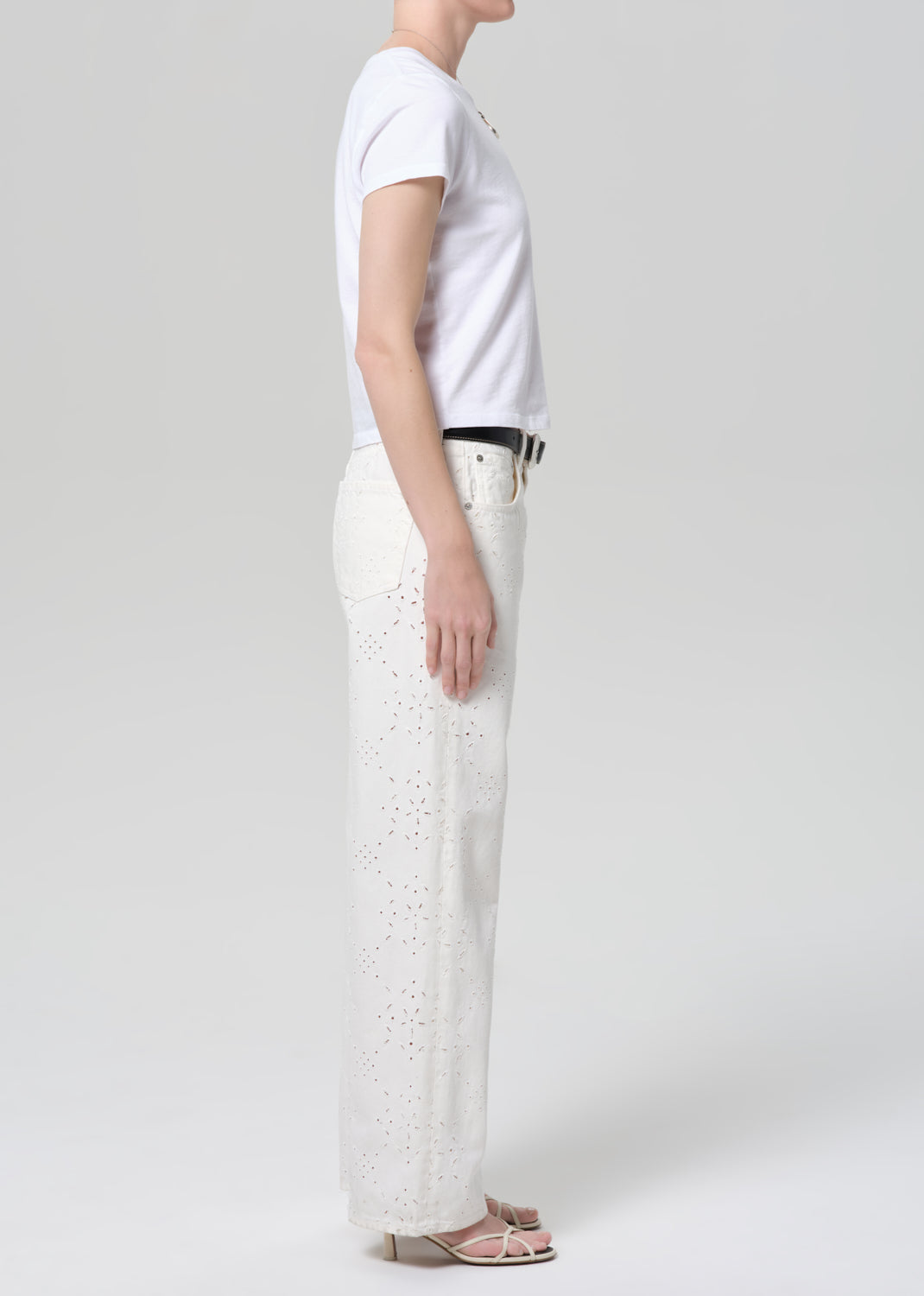 Person wearing a white t-shirt and white jeans with eyelet on a plain background