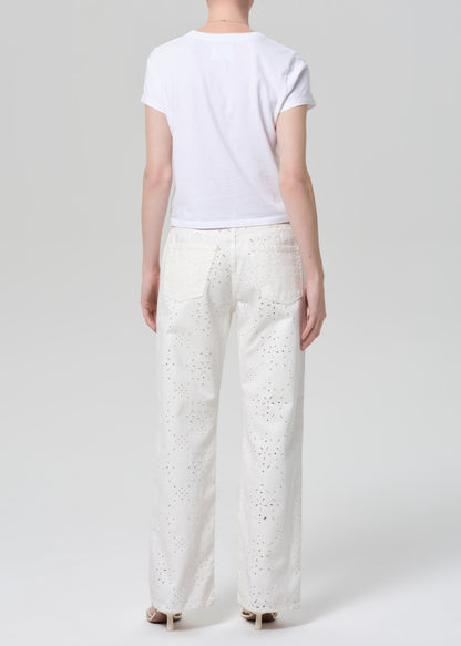 Person wearing a white t-shirt and white jeans with eyelet on a plain background