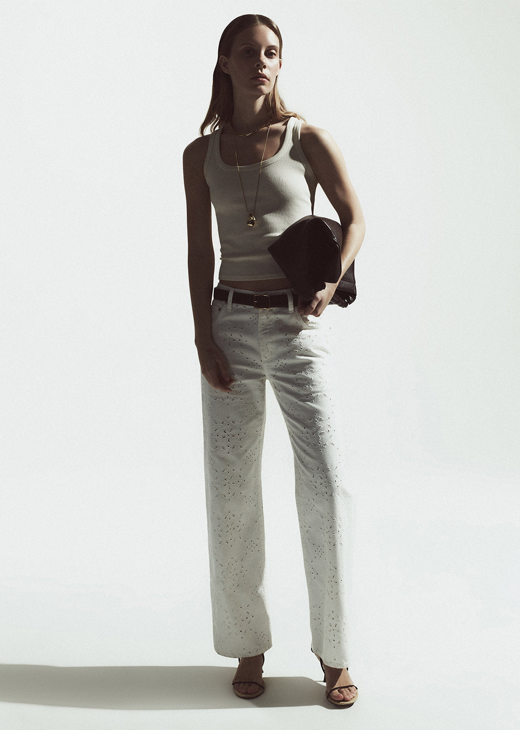 Woman wearing a white tank top and light-colored pants against a white background