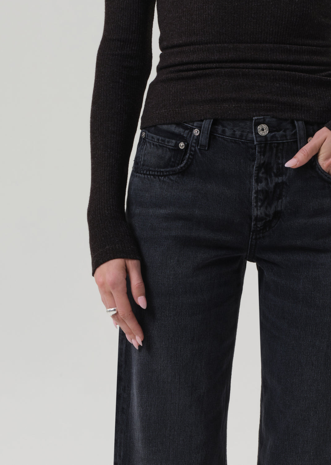 Person wearing black jeans and a brown top on a grey background
