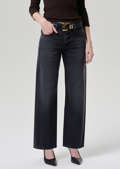 A model wearing dark charcoal wide-leg jeans with a gold-tone belt, paired with a dark brown top and black heels, shown from the waist down on a grey background.