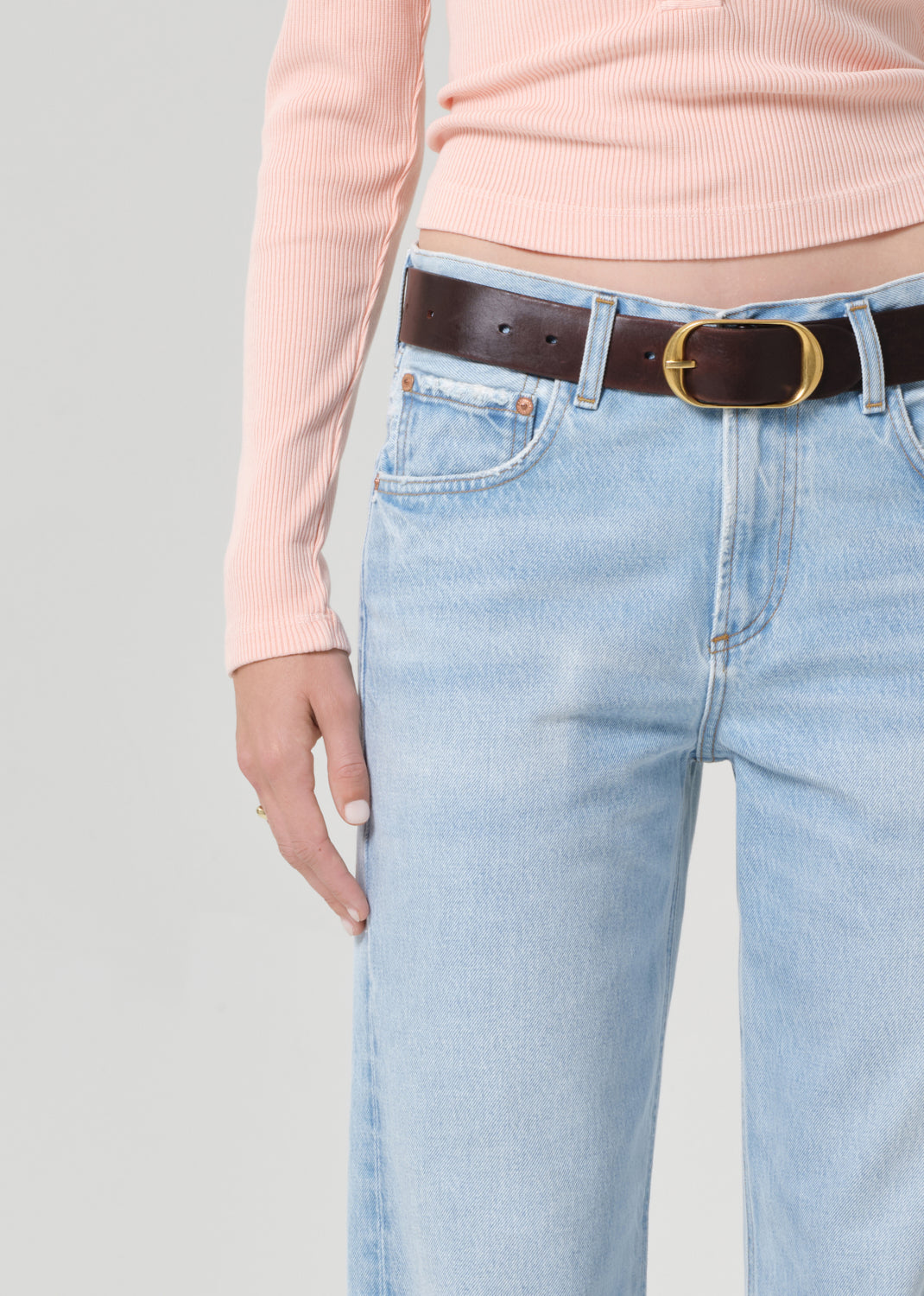 Person wearing a light pink long-sleeve shirt and light blue jeans on a grey background